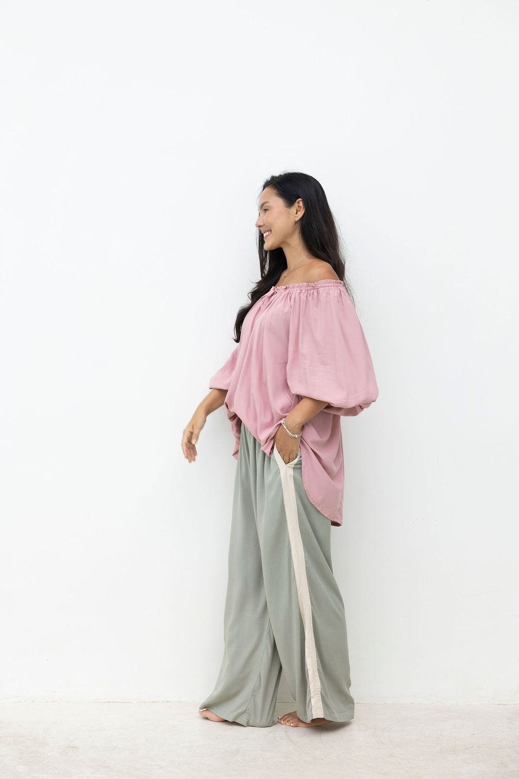 Woman wearing a pink off-shoulder top and gray pants with a white background