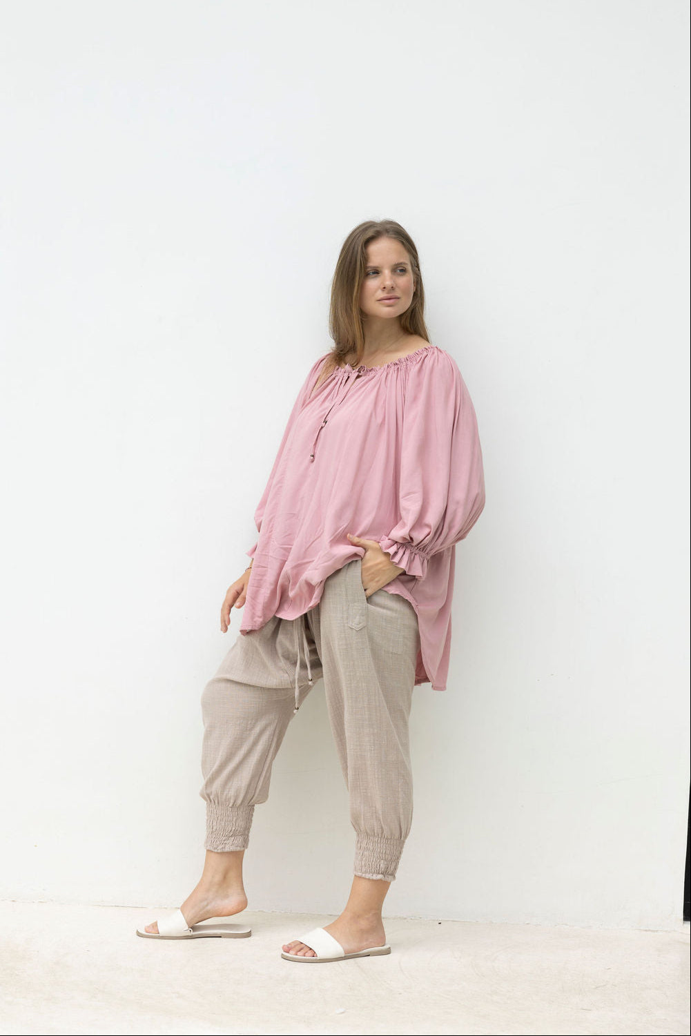 Woman wearing a pink blouse and beige pants against a white background