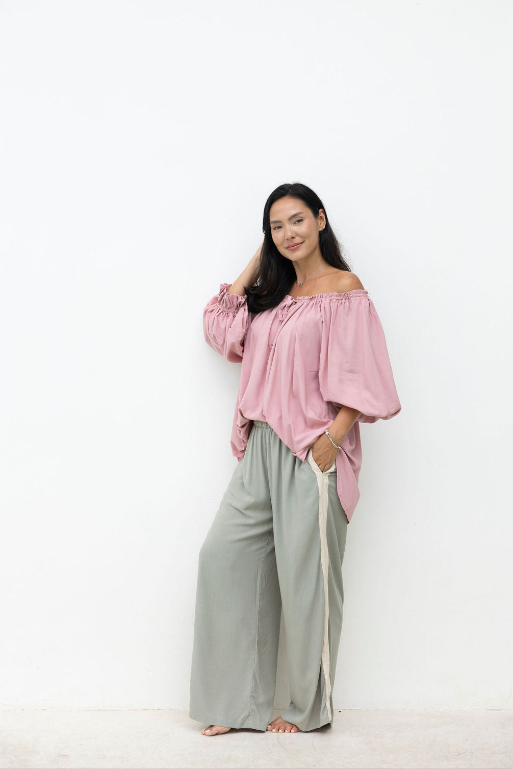 Woman wearing a pink off-shoulder top and light gray pants on a white background