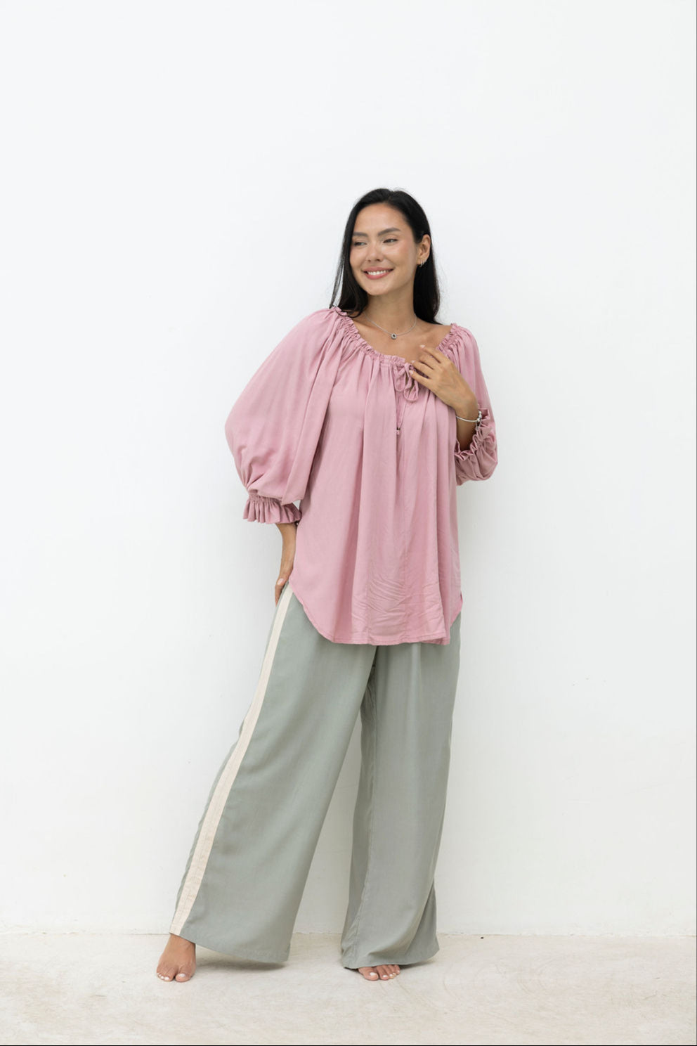 Woman wearing a pink blouse and gray pants with a white background