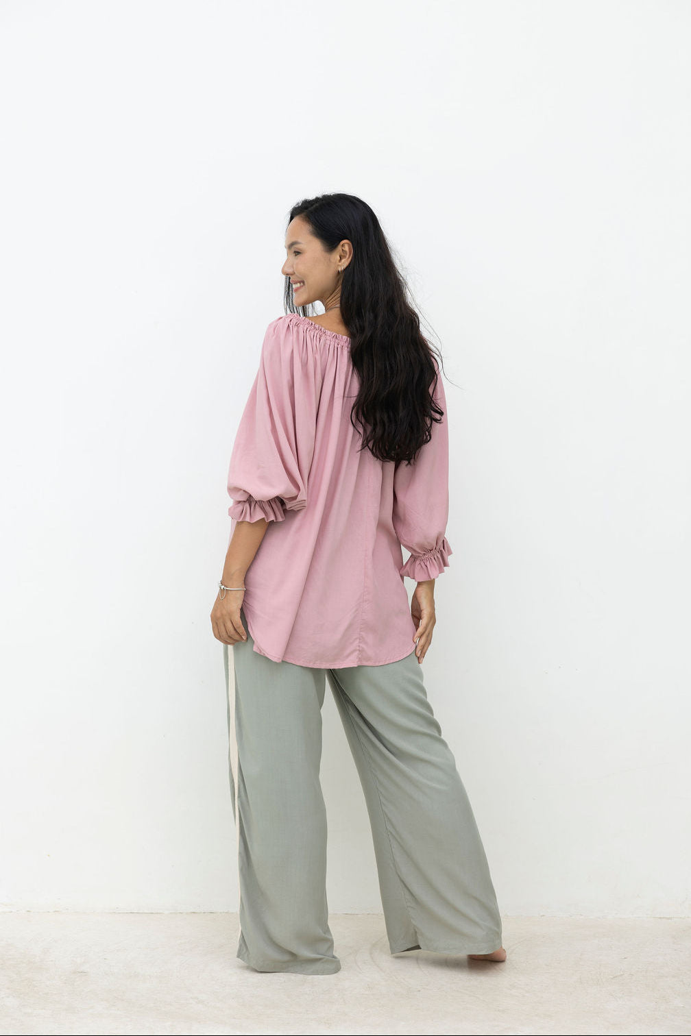 Woman wearing a pink blouse and gray pants on a white background