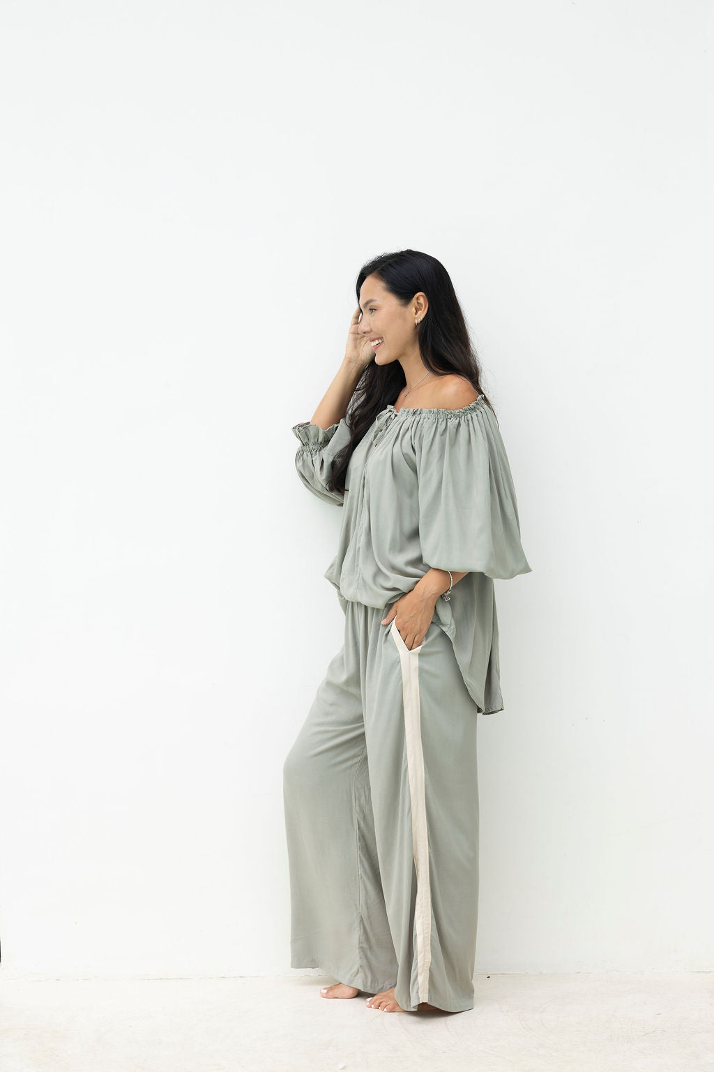 Woman wearing a light green off-shoulder top and wide-leg pants against a white background