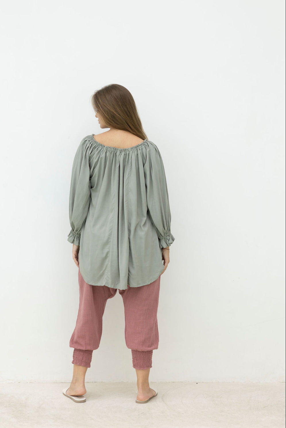Woman wearing a green off-shoulder top and pink pants against a white background