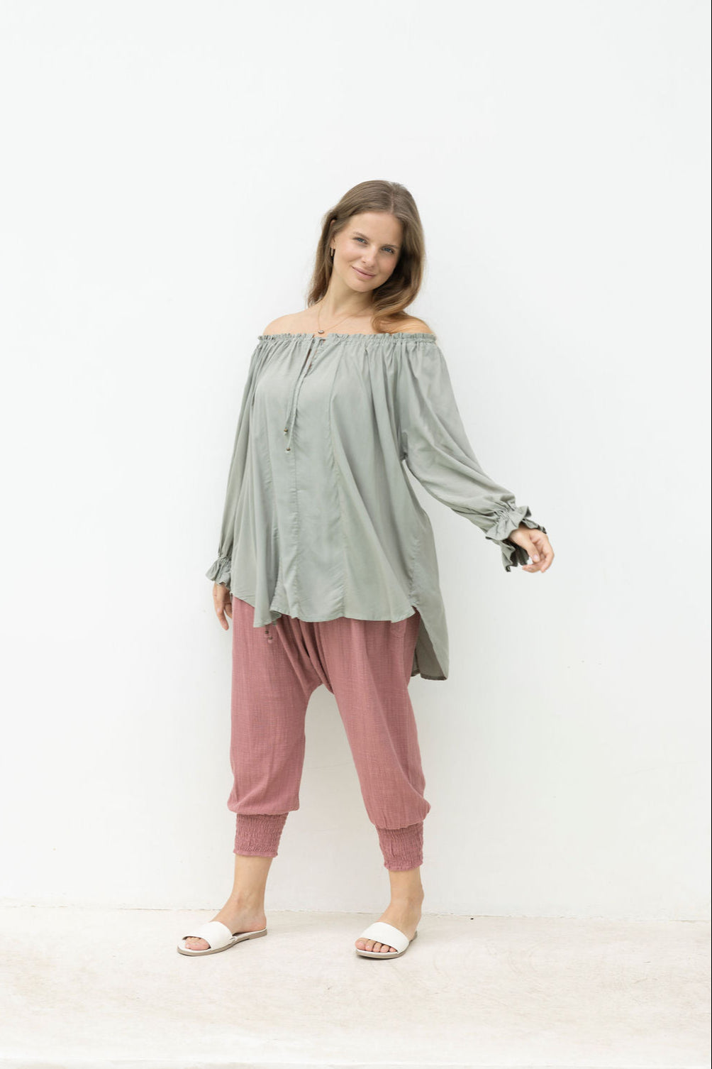 Woman wearing a light green off-shoulder top and pink pants on a white background