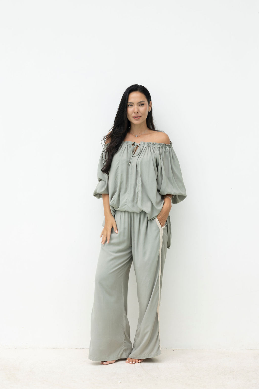 Woman wearing a light gray off-shoulder top and wide-leg pants on a white background