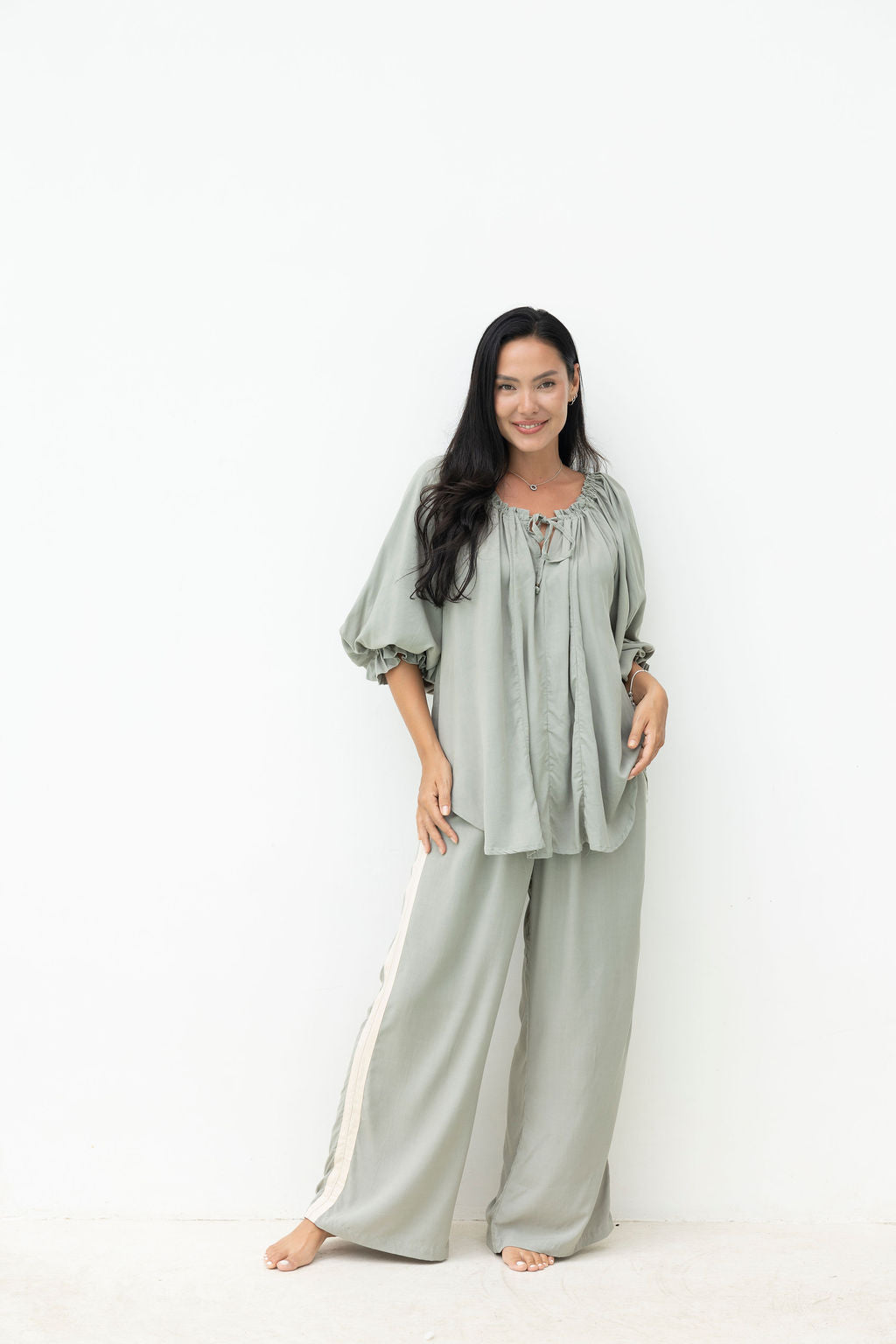 Woman wearing a light gray outfit with long sleeves and wide-leg pants on a white background
