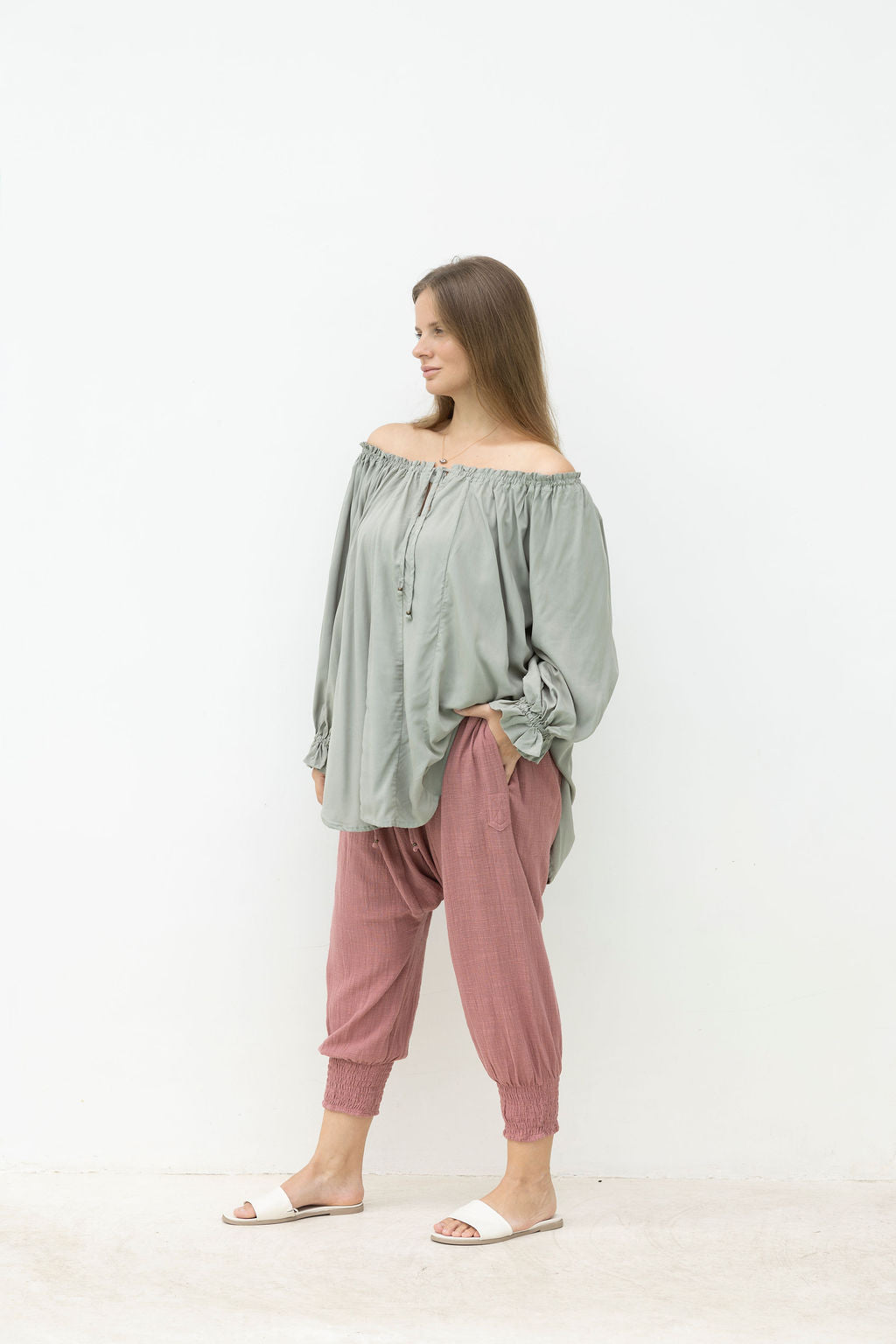 Woman wearing a light green off-shoulder top and pink pants on a white background