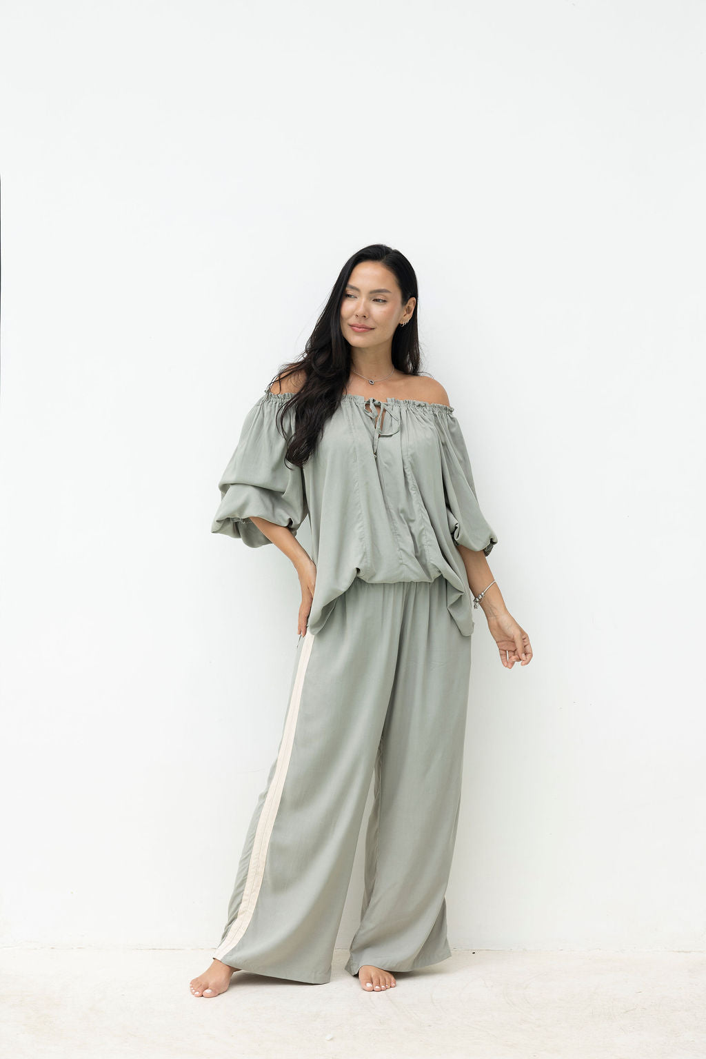 Woman wearing a light green off-shoulder top and wide-leg pants with a stripe on a white background