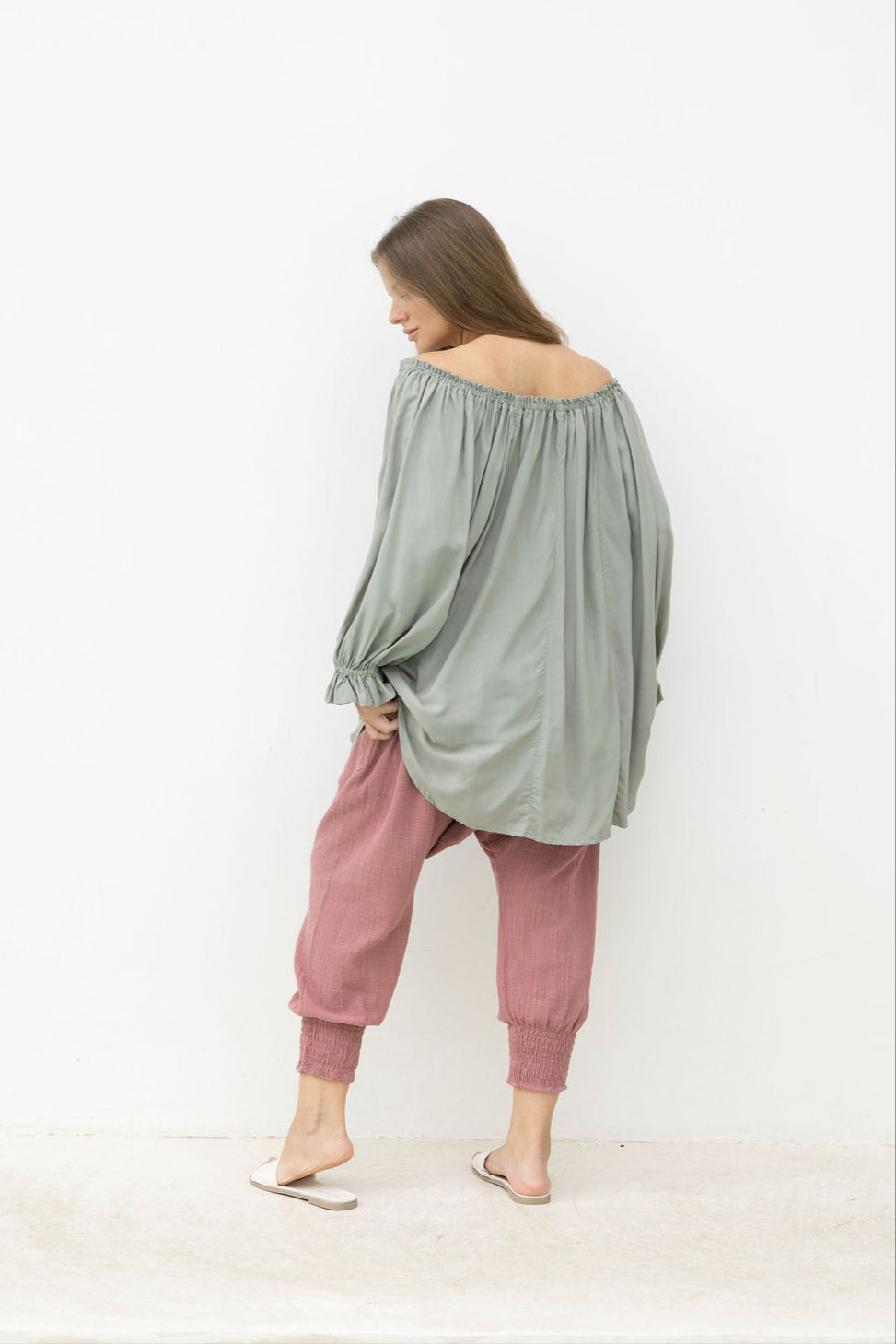Woman wearing a loose-fitting green top and pink pants against a white background