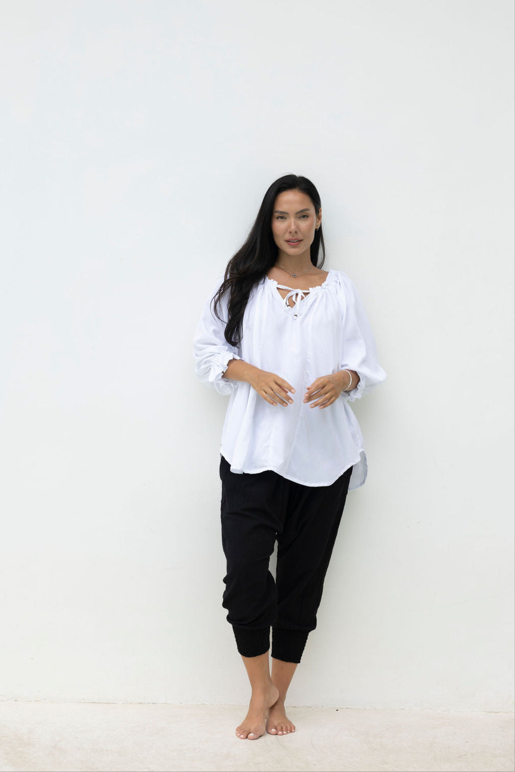 Woman wearing a white blouse and black pants against a white background