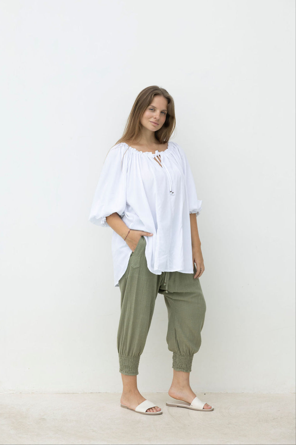 Woman wearing a white blouse and green pants against a white background