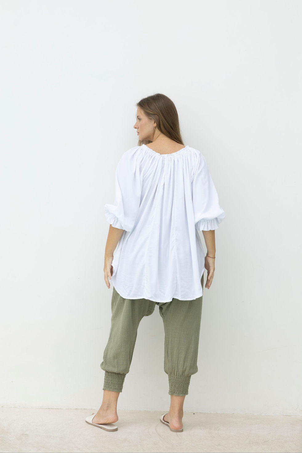 Person wearing a white top and green pants against a plain background