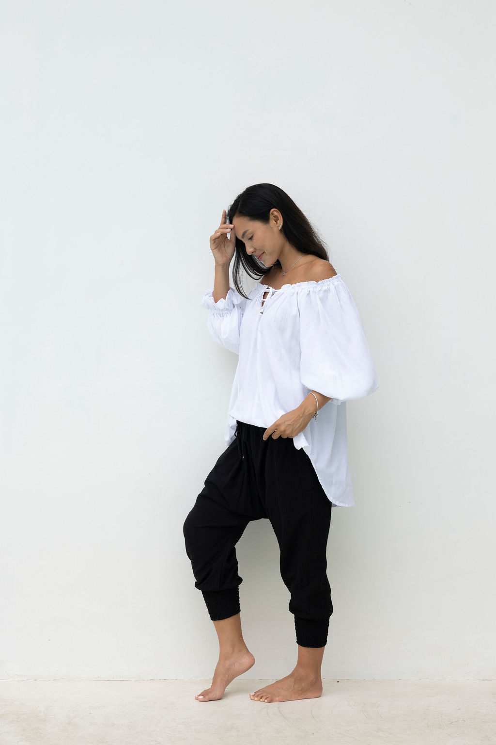 Woman wearing a white off-shoulder top and black pants against a plain background