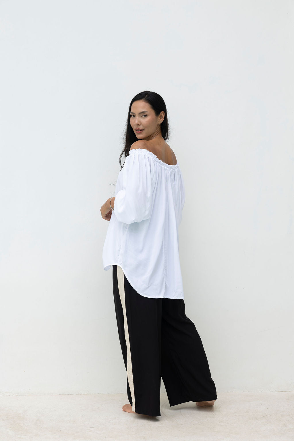 Woman wearing a white off-shoulder top and black pants with a stripe on a white background