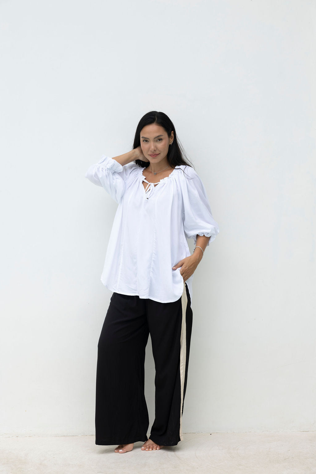 Woman wearing a white blouse and black pants against a plain background