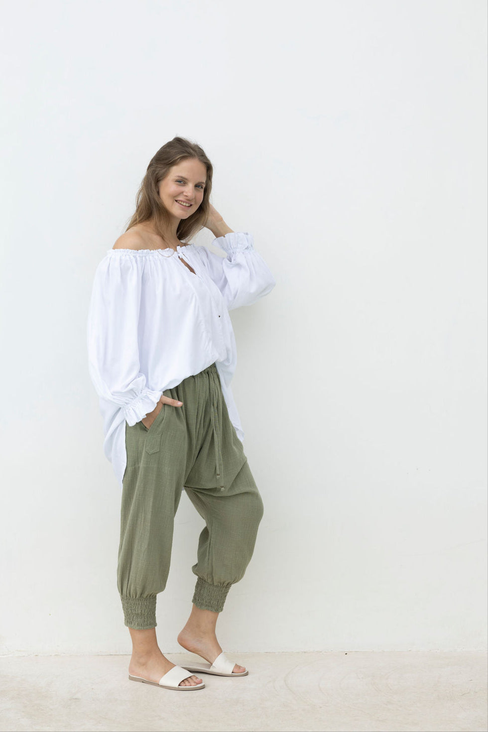 Woman wearing a white off-shoulder top and green pants against a white background