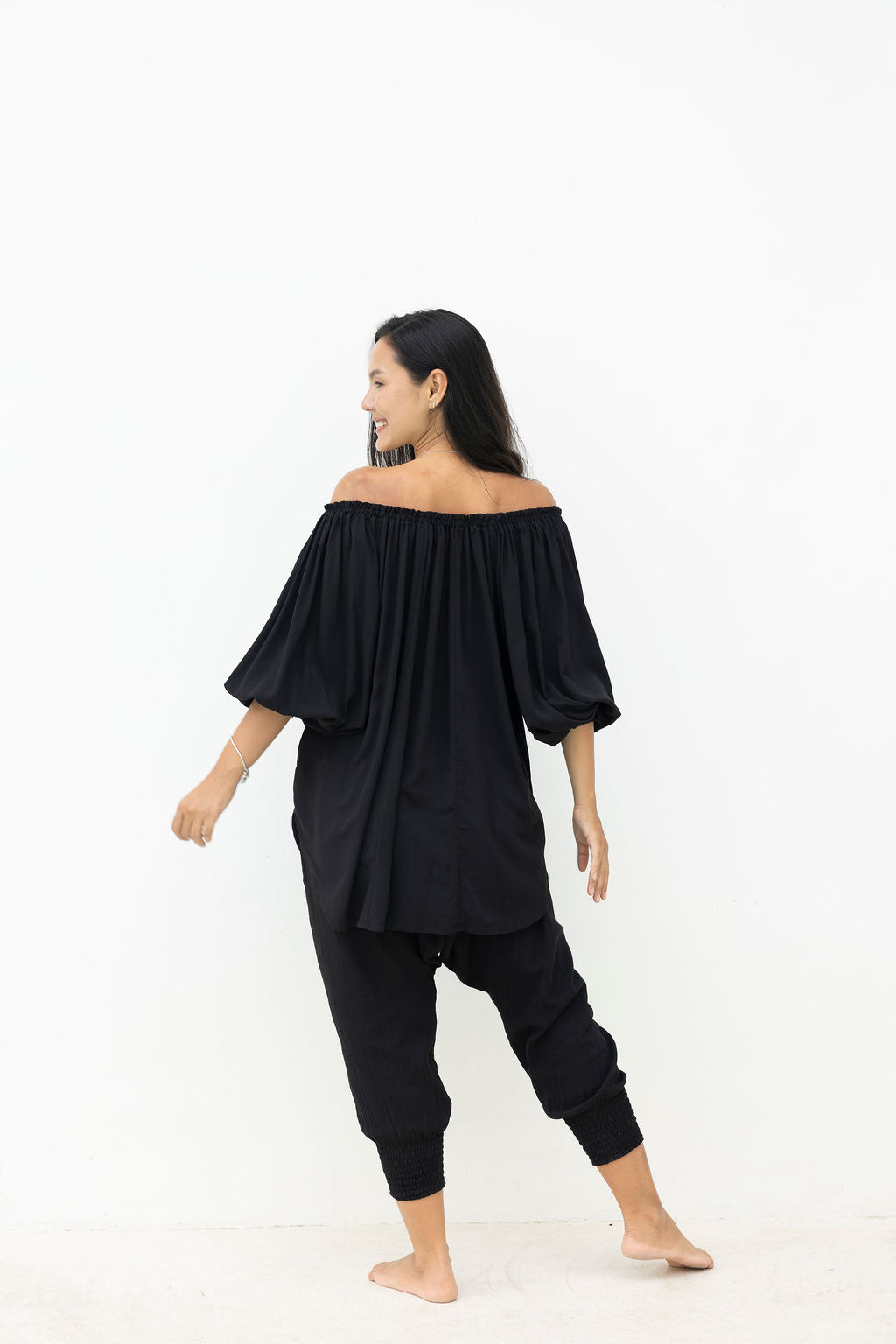 Woman wearing a black off-shoulder top and harem pants on a white background
