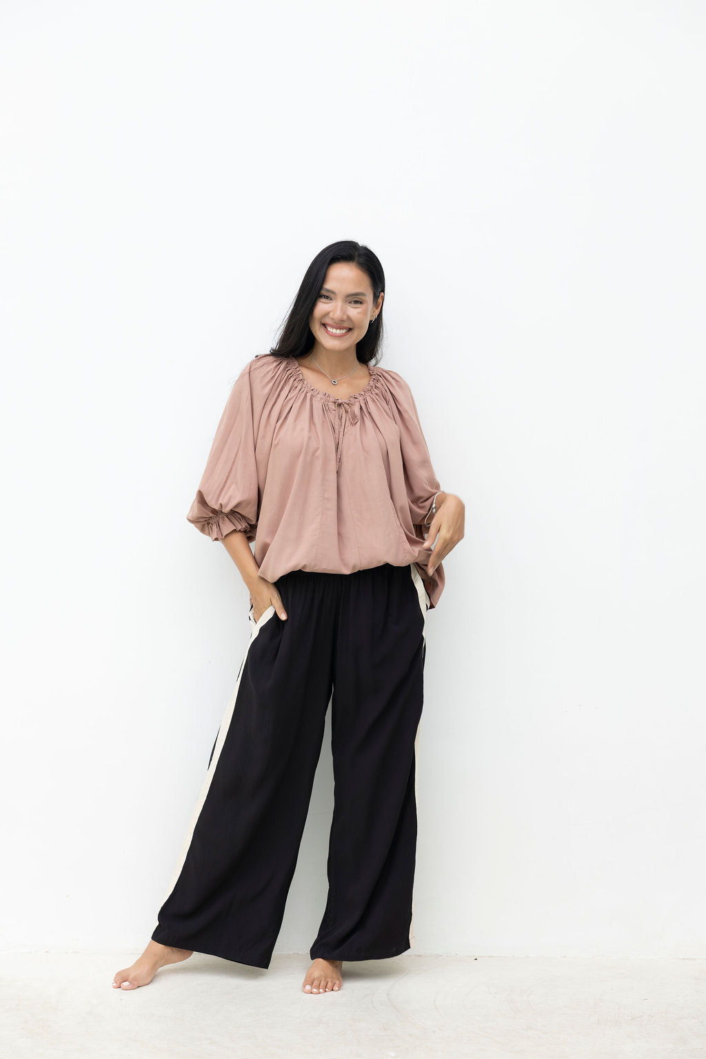 Woman wearing a pink top and black pants on a white background