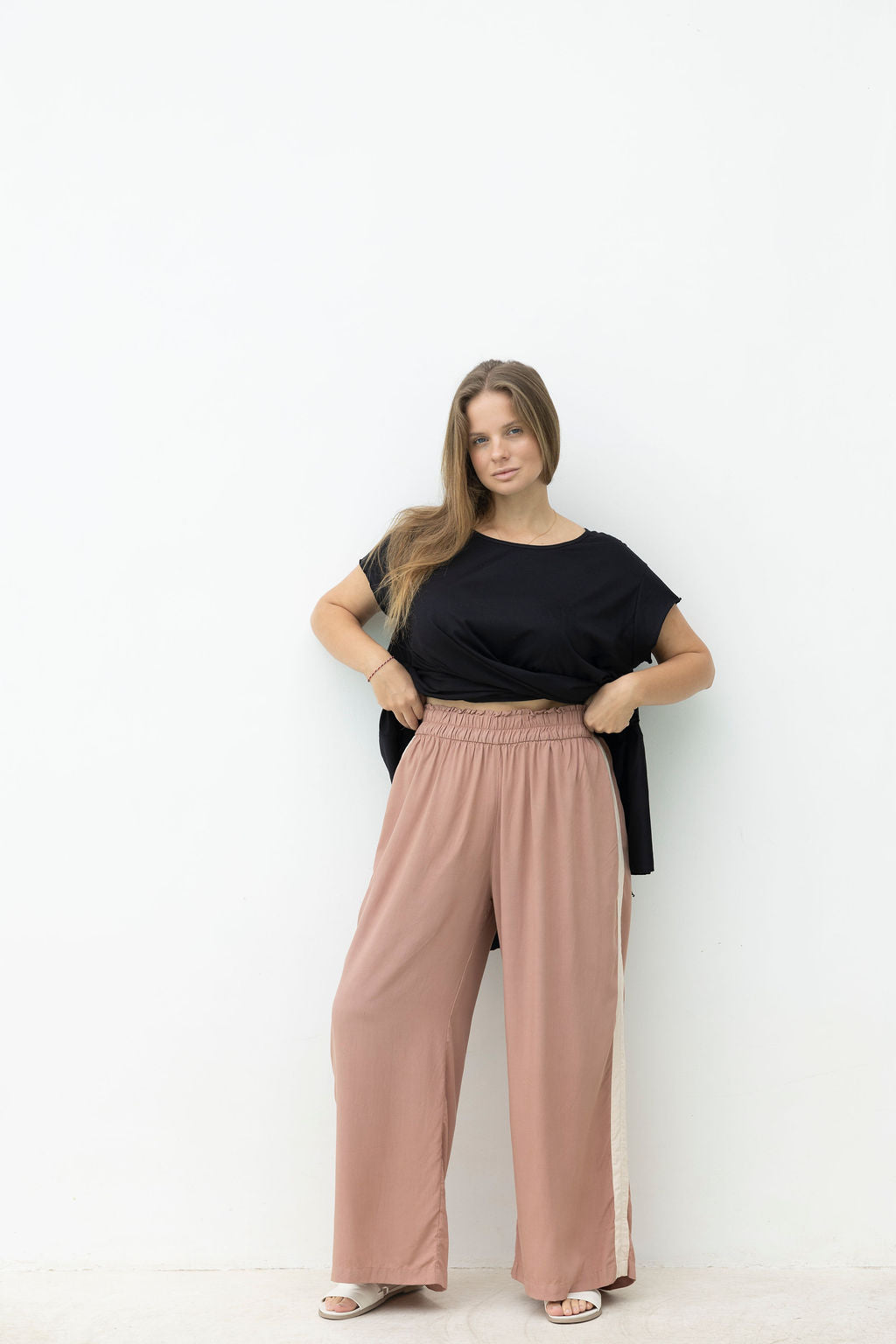 Woman wearing a black top and pink pants against a white background
