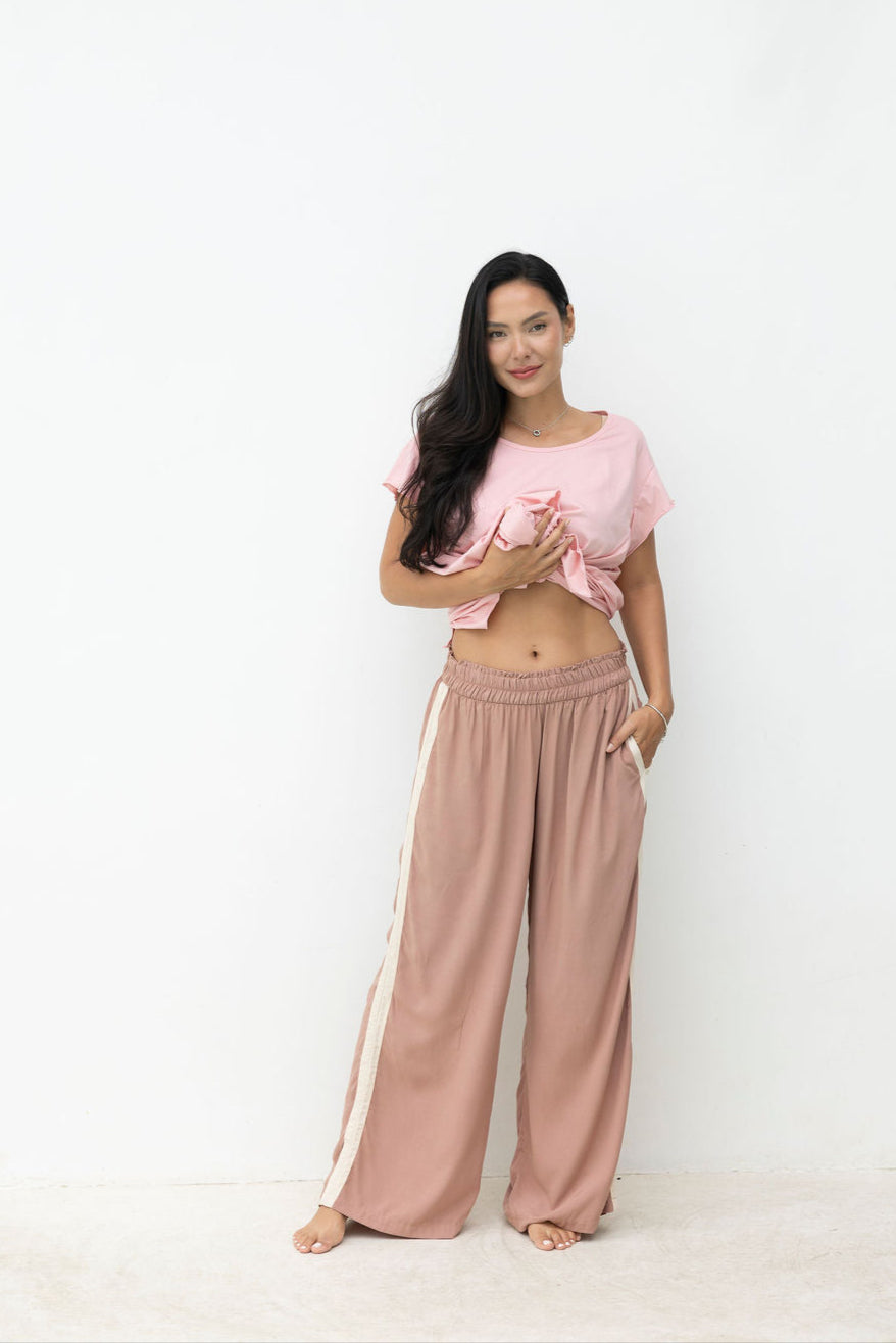 Woman wearing a pink top and beige pants with white stripes on a white background