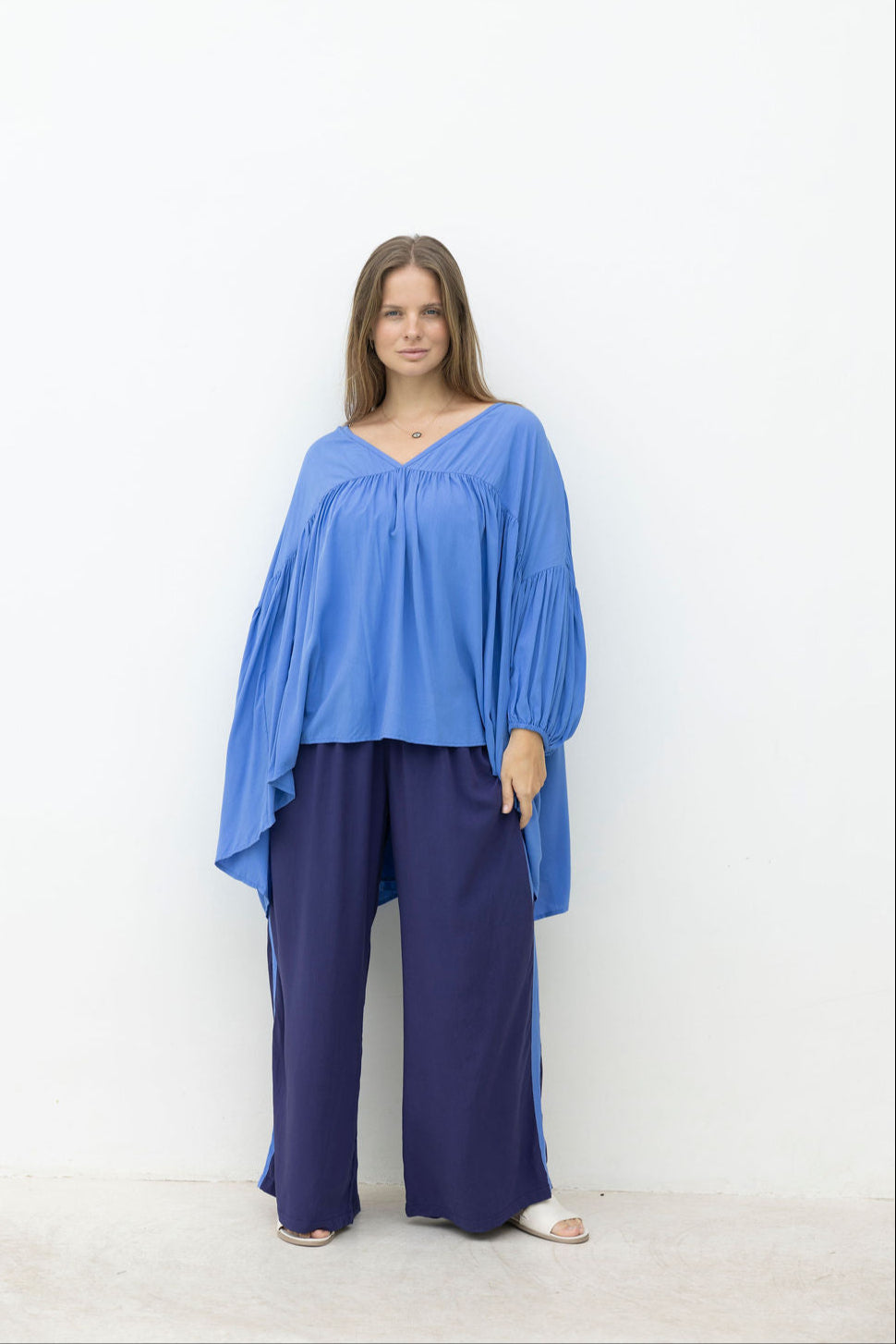 Woman wearing a blue top and dark pants on a white background