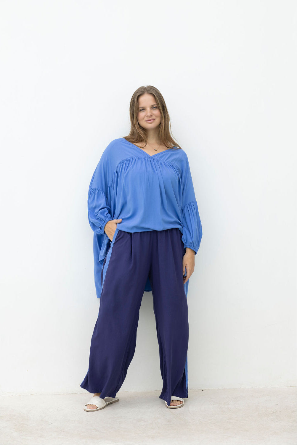 Woman wearing a blue top and dark pants against a white background