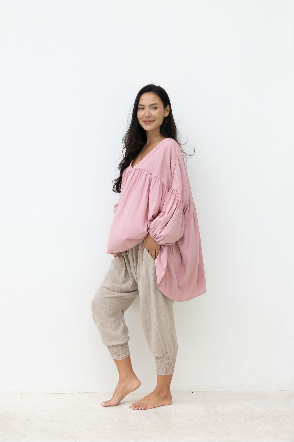 Woman wearing a pink oversized top and beige pants against a white background