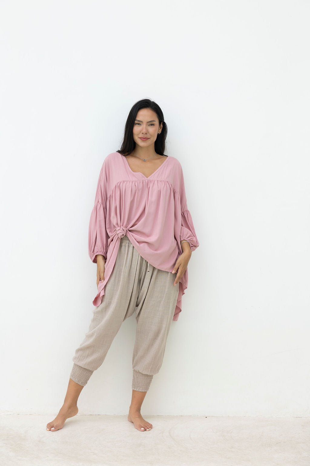 Woman wearing a pink top and beige pants on a white background