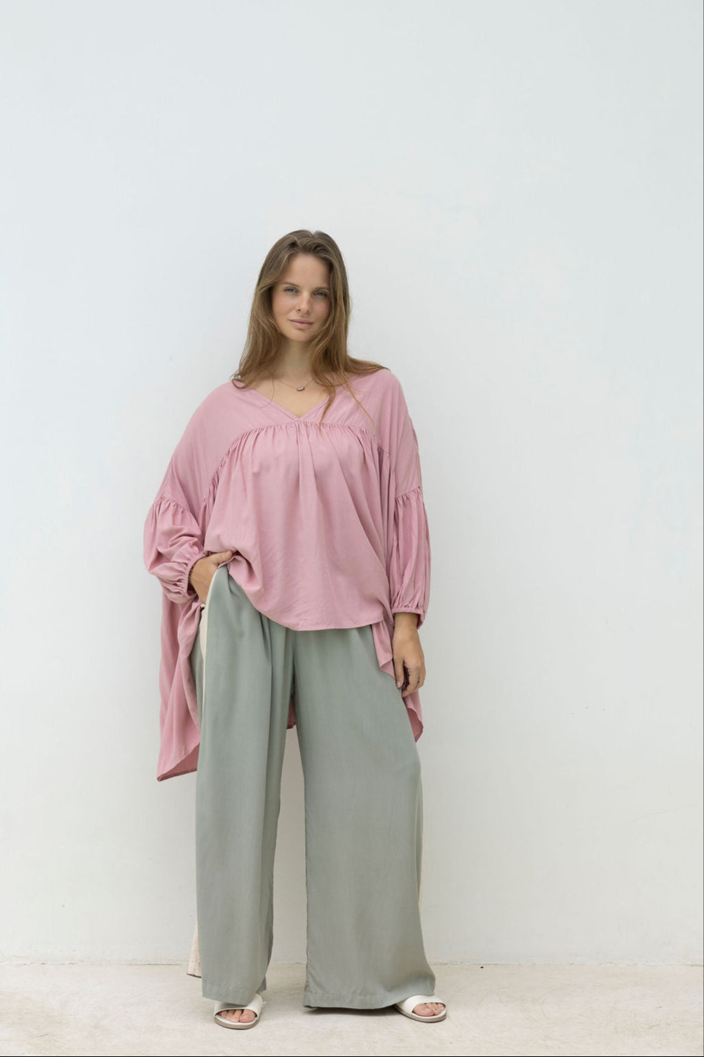 Woman wearing a pink blouse and light green pants against a white background