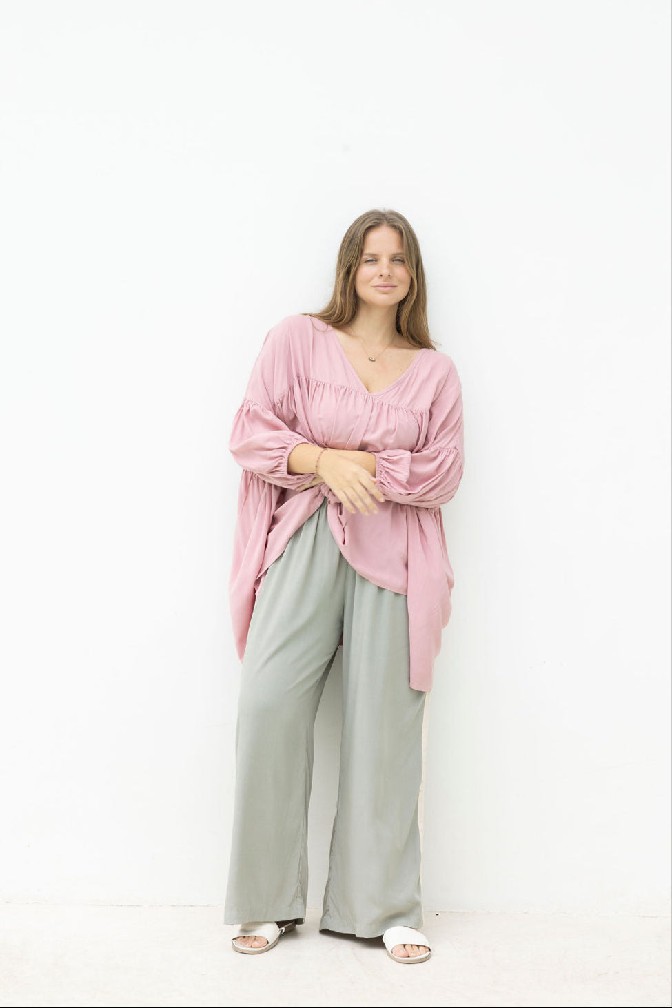 Woman wearing a pink blouse and light green pants against a white background