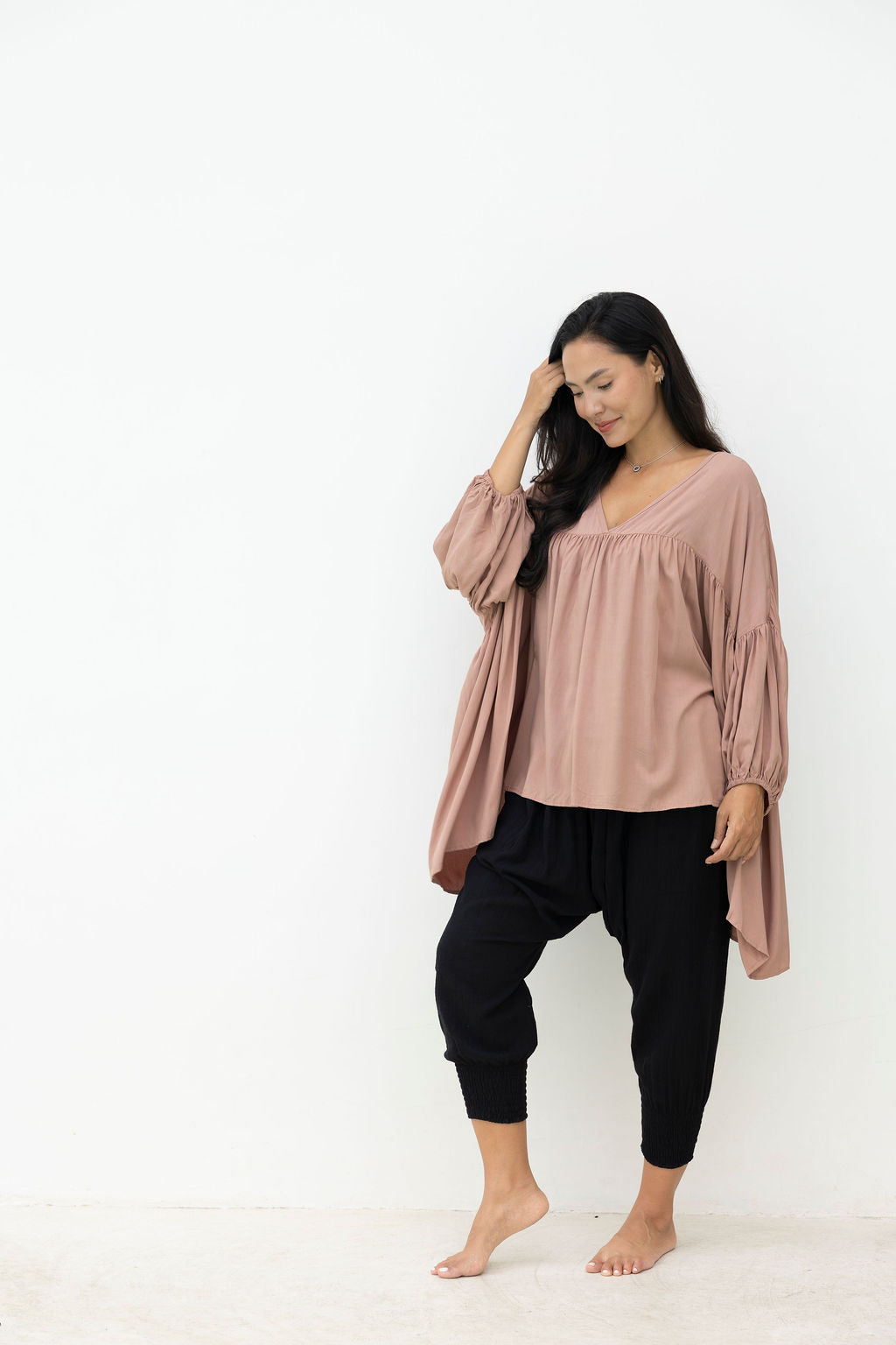 Woman wearing a mocca blouse and black pants against a white background
