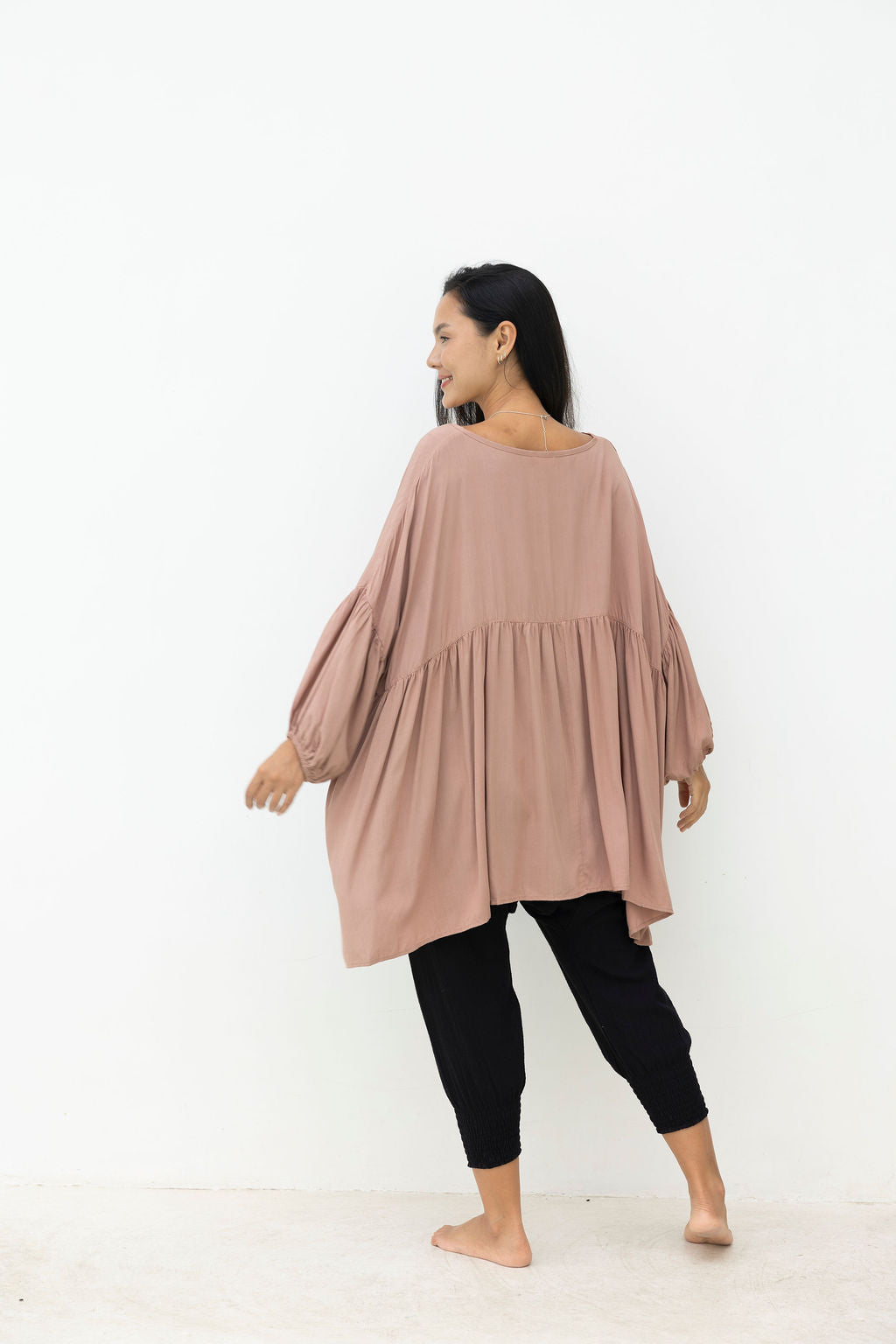 Woman wearing a mocca blouse and black pants against a white background