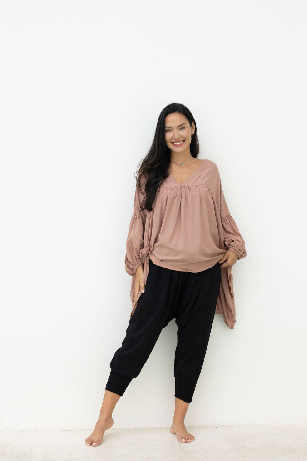 Woman wearing a mocca blouse and black pants against a white background