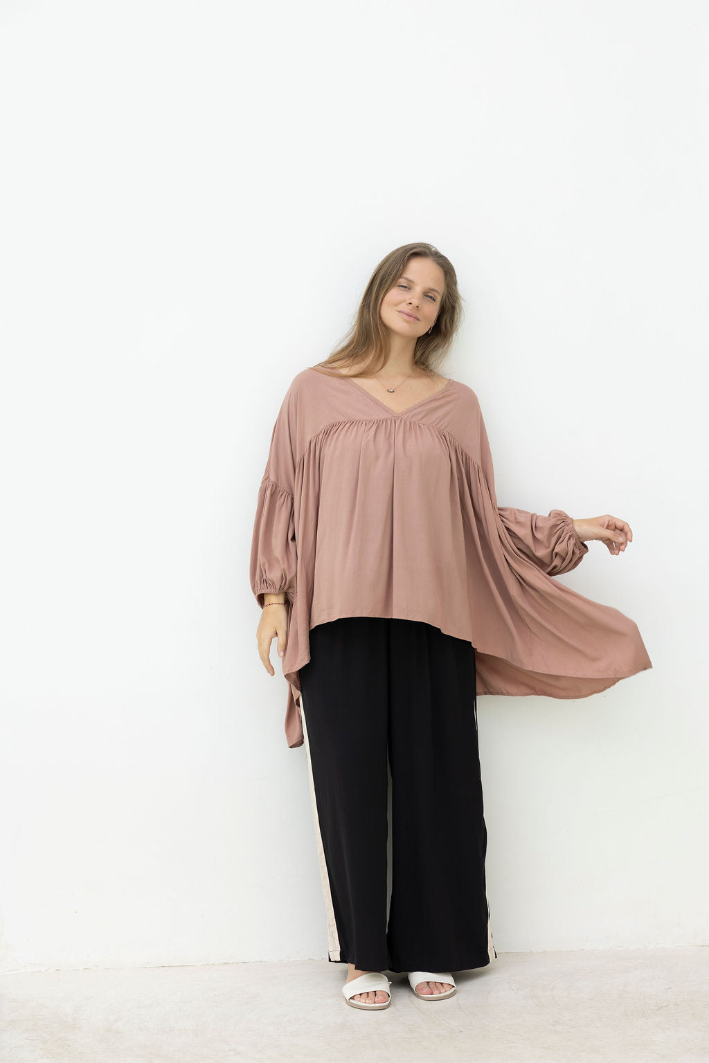 Woman wearing a mocca blouse and black pants against a white background