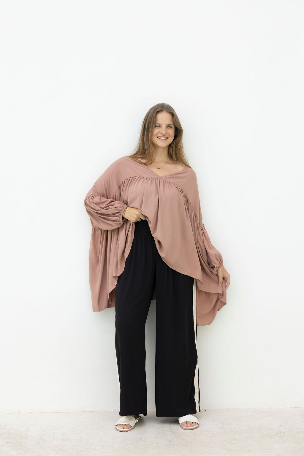 Woman wearing a mocca blouse and black pants against a white background