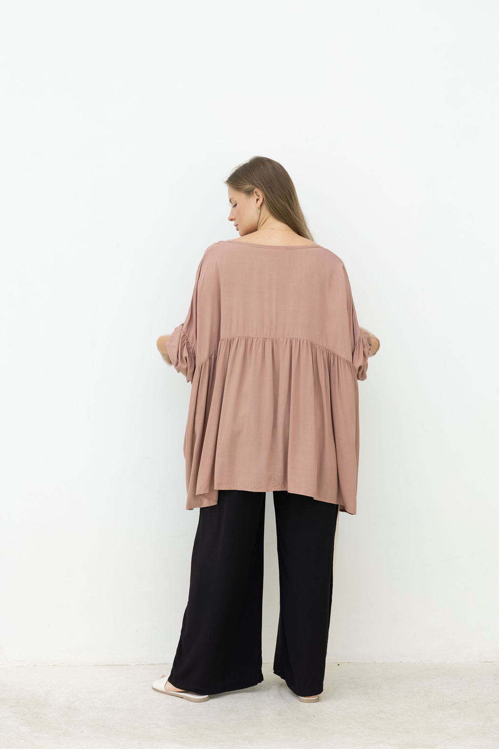 Woman wearing a mocca blouse and black pants against a white background