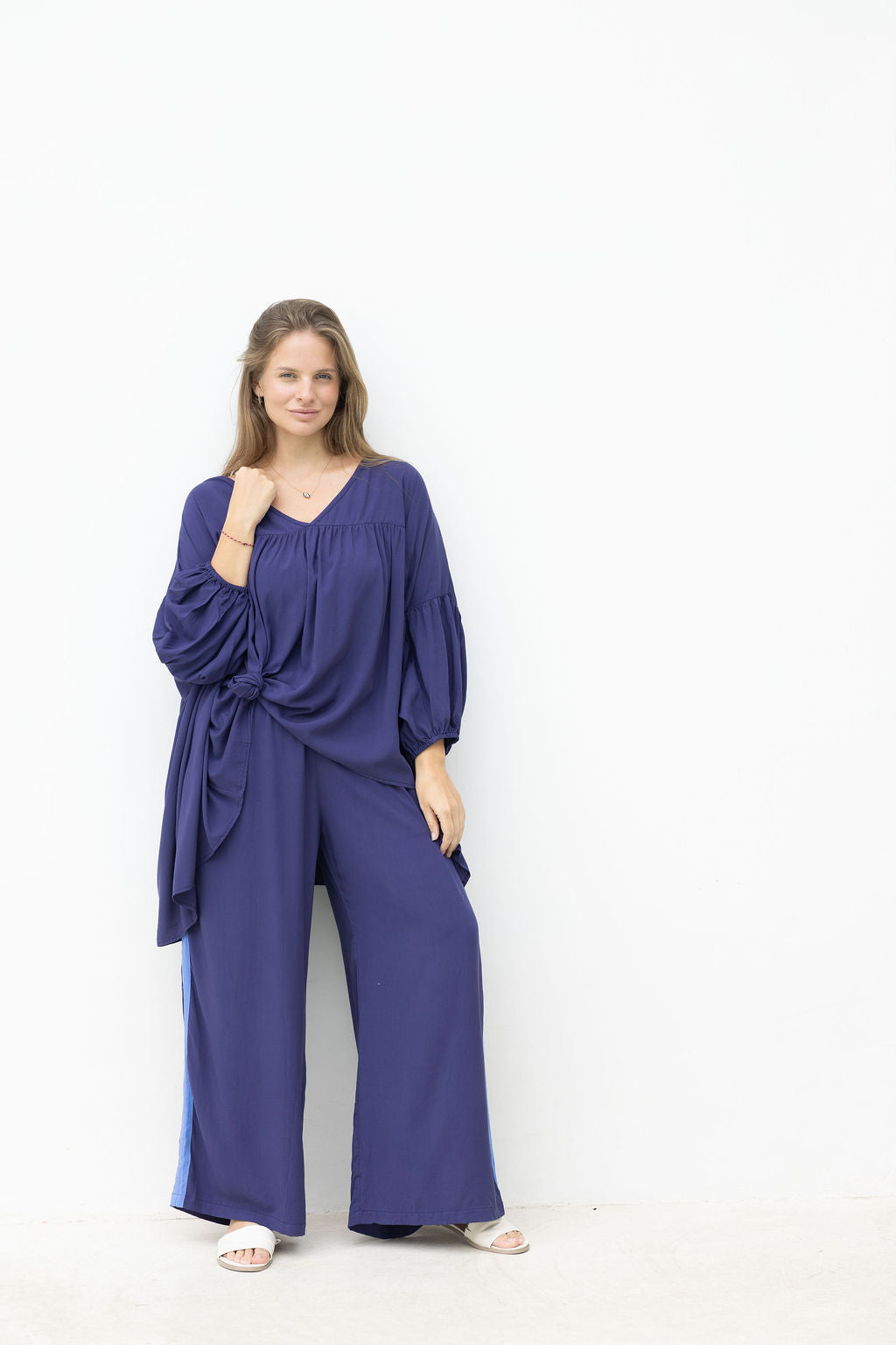 Woman wearing a long navy top with a pant with a blue stripe on the side on a white background