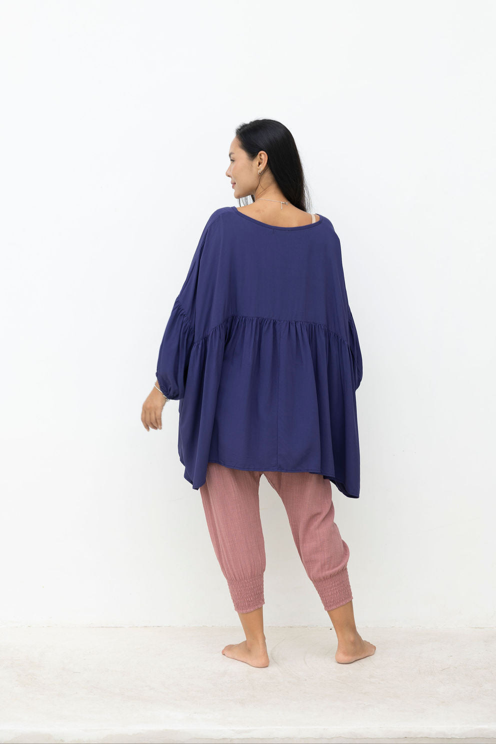 Woman wearing a long navy top with a dusty pink pant on a white background