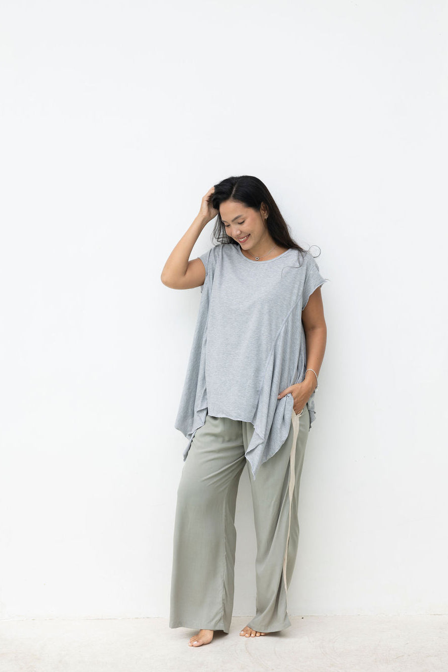 Woman wearing a light gray sleeveless top and beige pants against a white background