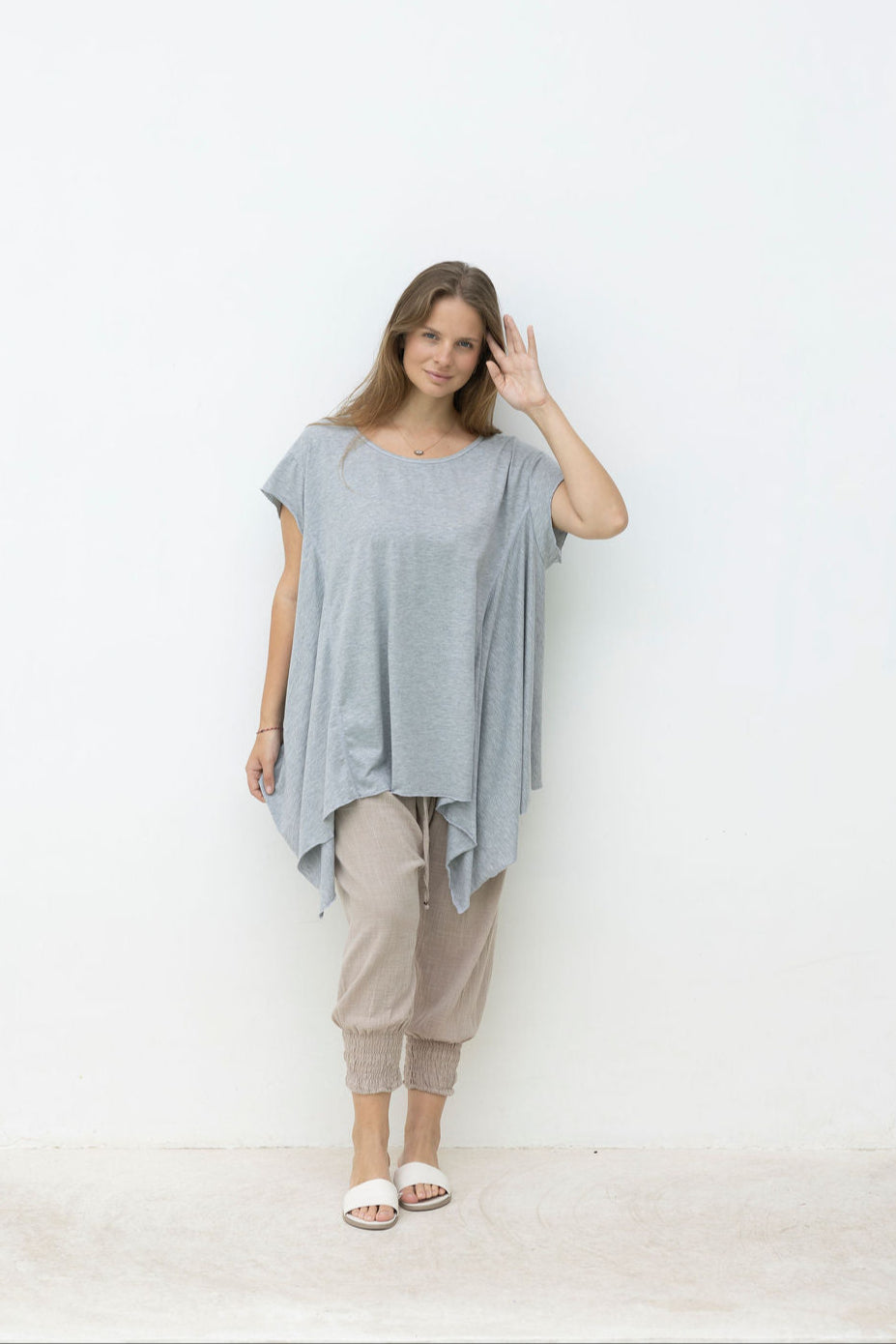 Woman wearing a light gray tunic and beige pants standing in front of a mirror.