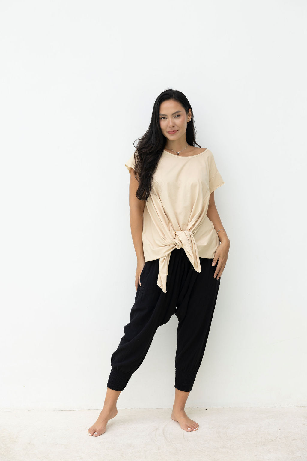 Woman wearing a beige top and black pants on a white background