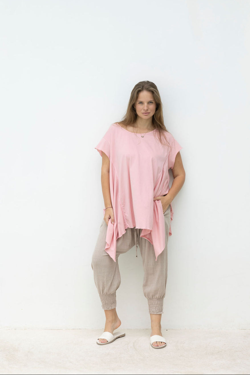 Woman wearing a pink oversized top and beige pants standing against a white wall.