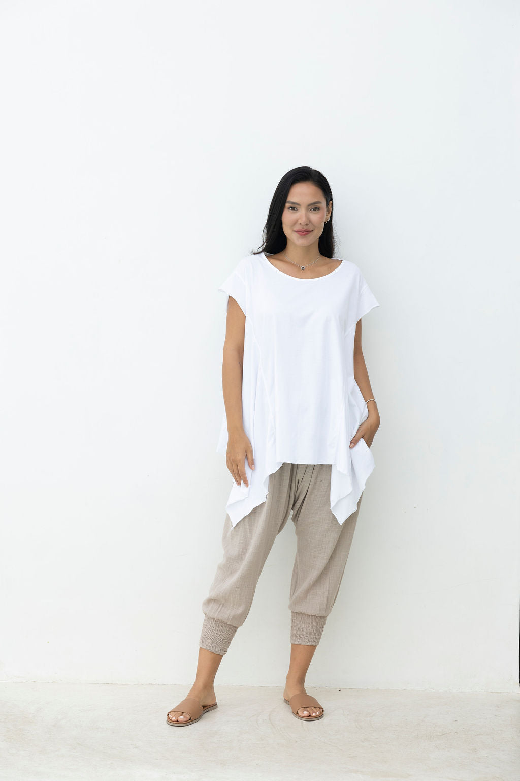 Woman wearing a white top and beige pants against a white background