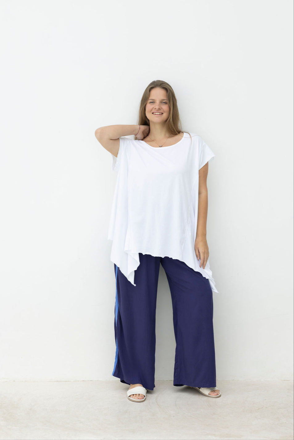 Woman wearing a white top and navy pants against a white background