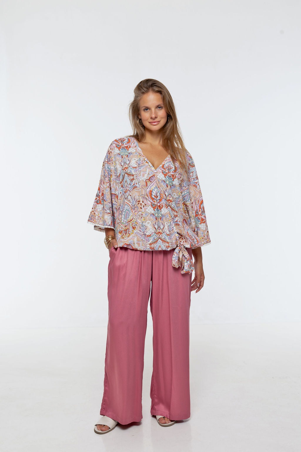 Woman wearing the Messina Top - Palazzo Print.  A flowing printed rayon top with a wrap-over neckline, kimono sleeves, crochet trim, elastic waist with adjustable tie