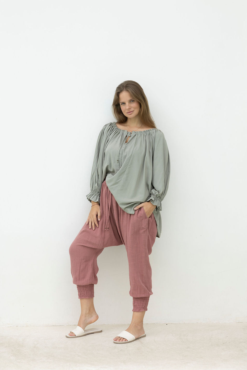 Woman wearing a green top and pink pants against a white background