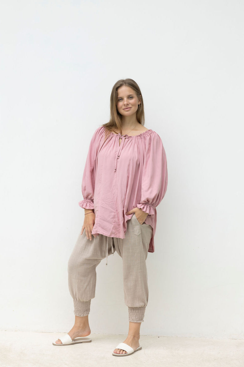 Woman wearing a pink blouse and beige pants on a white background