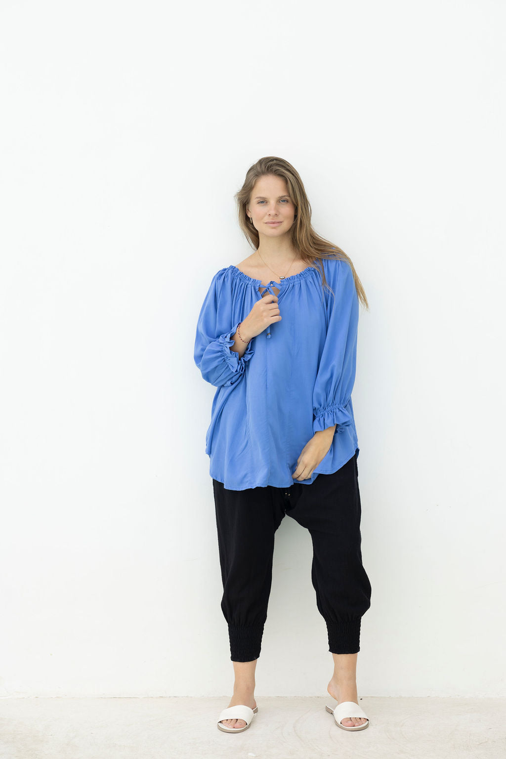 Woman wearing a blue blouse and black pants against a white background