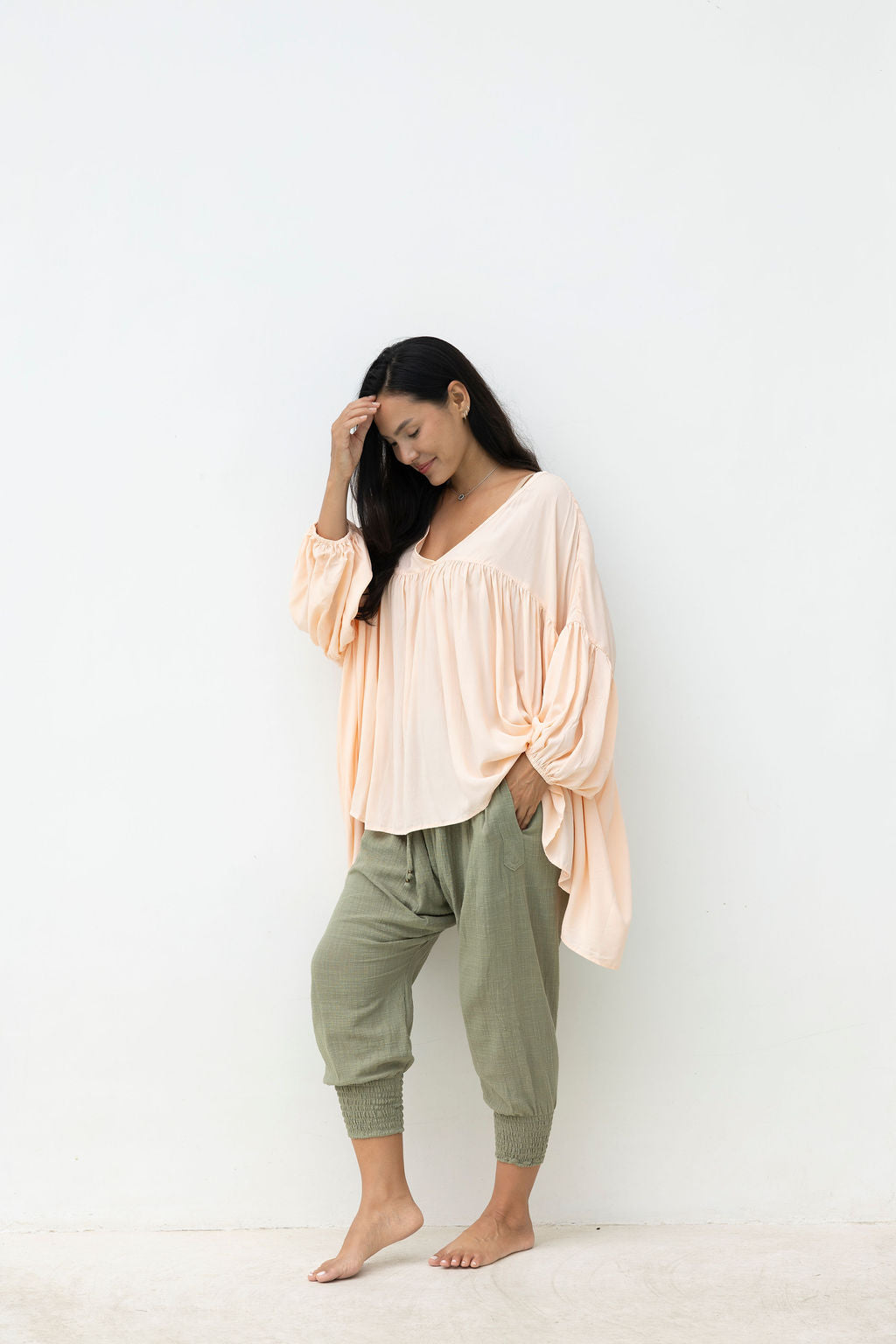 Woman wearing a light pink top and green pants against a white background