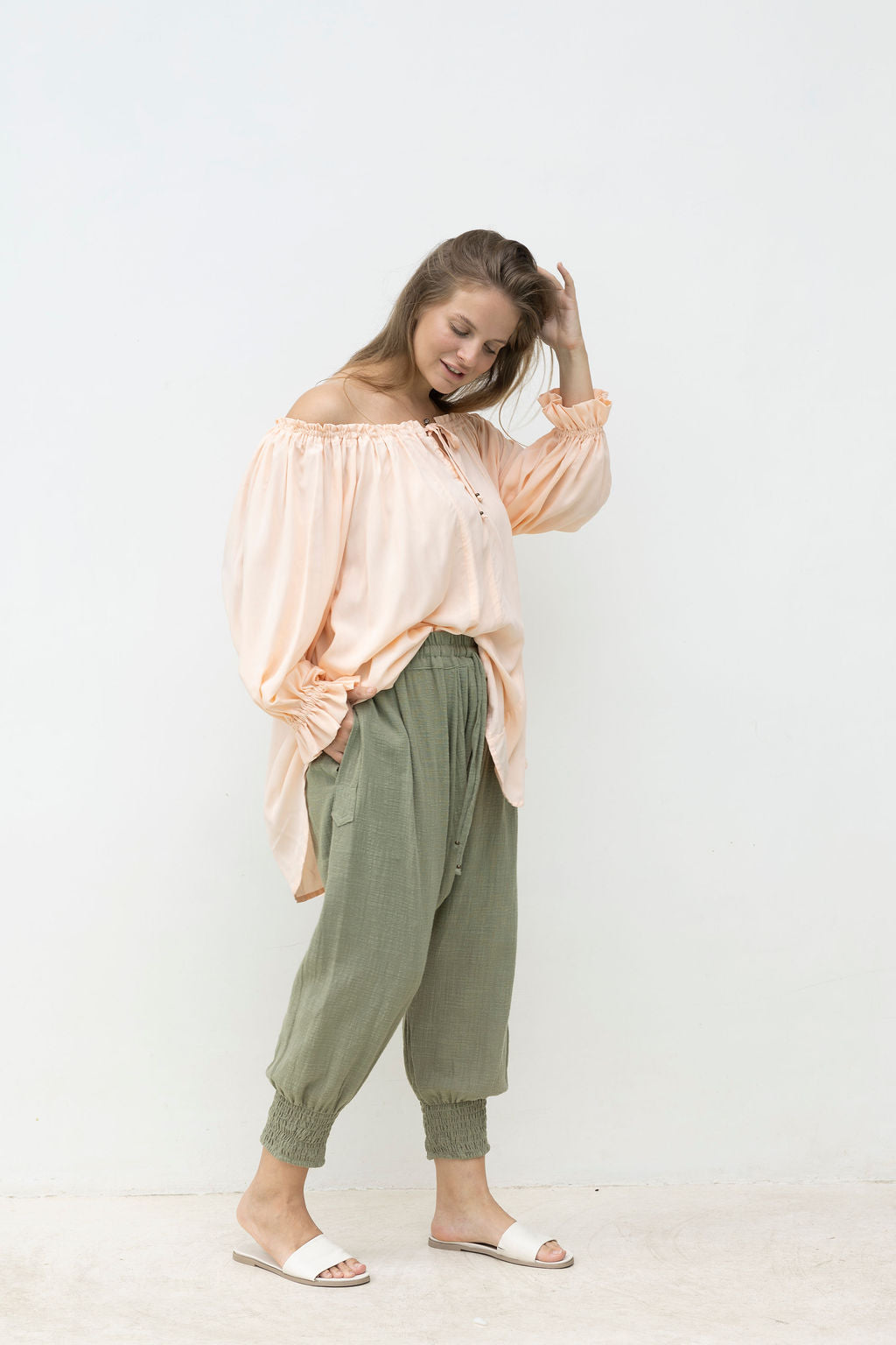 Woman wearing a light pink off-shoulder top and green pants on a white background